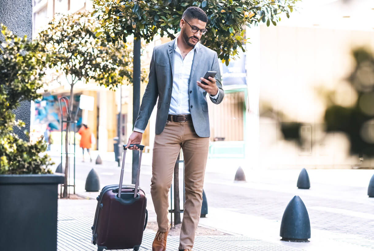 Photo of a man walking with a suitcase using a smart phone