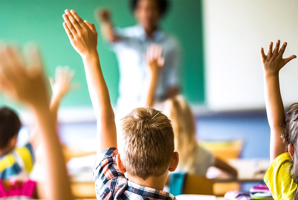 A classroom where the students are all raising hands