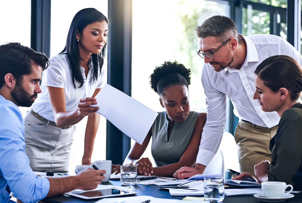 Photo of a group of people working around a table covered in papers